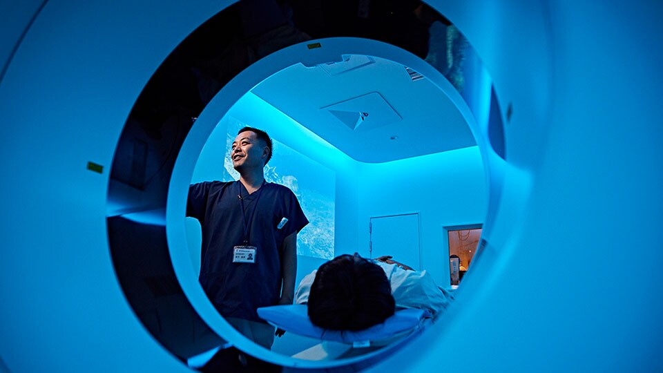 Fotografía de un médico configurando una exploración en el gantry del escáner de TAC, con el paciente sobre la mesa de paciente del sistema de TAC