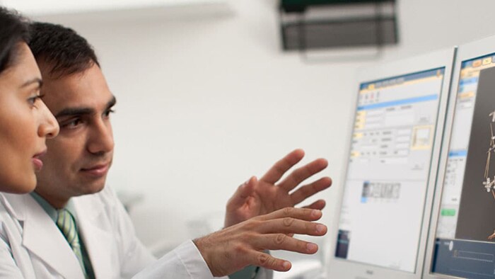Foto de médicos deliberando sobre los resultados de una TAC en un monitor de ordenador