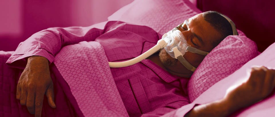 Hombre vestido de rosa que duerme con una mascarilla