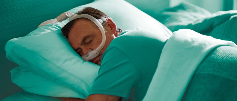 Hombre con camiseta verde y mascarilla que duerme boca abajo